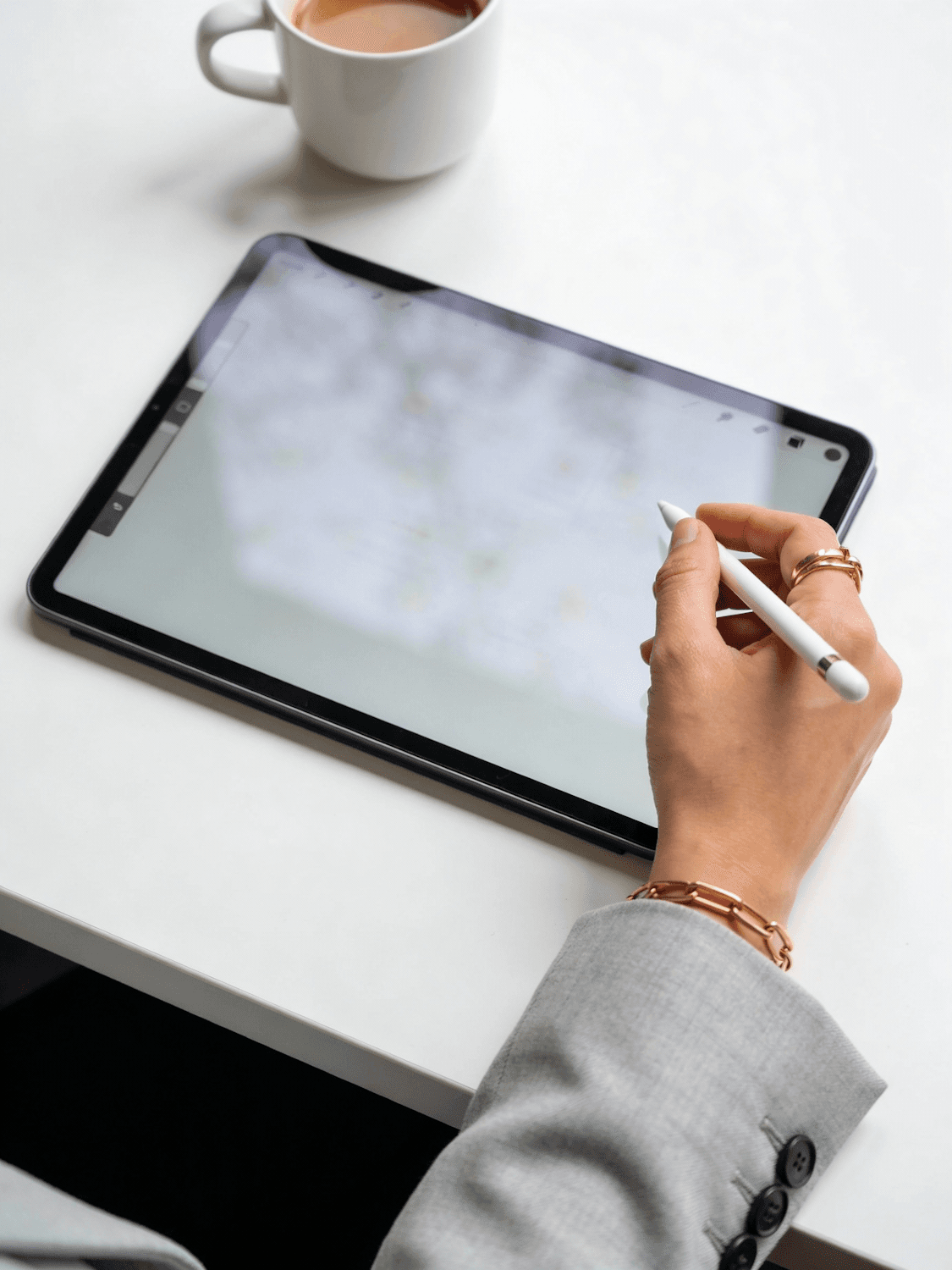 Hand mit Eingabestift auf einem Tablet, daneben eine Tasse Kaffee
